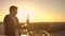 A male freelance programmer sits on a skyscraper roof with a laptop and beer typing code on a keyboard during sunset