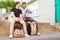 Male Gay Couple On Vacation Sitting On Wall With Backpacks Looking At Mobile Phone