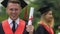 Male graduate in academic dress holding university diploma, smiling to camera