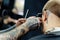 Male haircut with electric razor. Tattooed Barber makes haircut for client at the barber shop by using hairclipper. Man