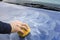 Male hand applies polishing paste on car paint with sponge