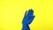 Male hand in blue glove is waving welcoming you against a yellow background.