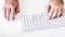 Male hand clicking on a mouse and typing on a white keyboard on a white table