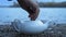 Male Hand Close-Up Pour Green Tea into White Porcelain Teapot Standing on the River Bank