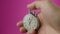 Male hand holding analogue stopwatch on pink background. Time start with old chronometer man presses start button in the