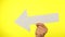 Male hand holding a big white arrow pointing left isolated on yellow background