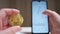 Male hand holding cryptocurrency coin and cell phone showing graph