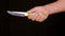 Male hand holding knife with sharp blade and wooden handle on black background