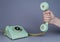 Male hand holding an old blue plastic telephone receiver near rotary telephone on gray background. Close up remote