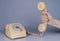 Male hand holding an old yellow plastic telephone receiver near rotary telephone on gray background. Close up remote