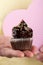 Male hand holding or presenting tasty appetizing chocolate cupcake. Yellow Background. Closeup.