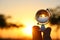 male hand holding small crystal globe in front of sunset