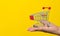 Male hand holding small shopping cart trolley over yellow background. Online shopping and fast delivery concept