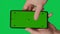 Male hand holding a smartphone with vertical green chroma key screen isolated on green background. Different signs and