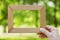 Male hand holding wooden frame against a blurred natural background. Empty space for text. Connecting with nature concept.