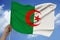 Male hand holds against the background of the sky with clouds the national flag of algeria on a luxurious texture of satin, silk
