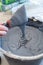 A male hand holds a spatula with the mixture over a bucket of freshly mixed mortar.