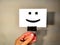 Male hand holds a white card on a background of a gray wall on a metal clothespin with a smile icon.