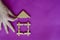 Male hand installs the roof on toy children wooden house on lilac background