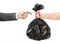 A male hand in a jacket transfers money to the other hand in exchange for a garbage bag