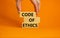 Male hand placing a blocks with word `code` on top of a blocks tower. Text `code of ethics`. Beautiful orange background. Copy