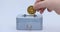 Male hand puts a cryptocoin, Ethereum or ETH, in a small grey vault, safe or piggy bank, depicting crypto or