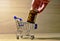 Male hand puts pills in the shopping cart on wood background. Medicine grade pharmaceutical tablets at mini shopping trolley.