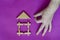 Male hand shares click with sticks on the roof of toy children wooden house on lilac background