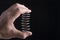 The male hand squeezes a metal spring on a black background