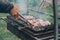 Male hand turns with tongs raw fried meat on skewers, cooked on charcoal grill. Cooking barbecue outdoors