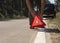 Male hands closeup putting red triangle caution sign on road side near broken car in summer