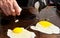 Male hands cracking open an egg, with two eggs frying on a flat grill