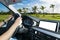 Male hands holding car steering wheel. Hands on steering wheel of a car driving near palm field. Man driving a car inside cabin.