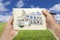 Male Hands Holding Paper With House Drawing Over Empty Grass Field