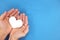 Male hands holding a white heart in blue background top view. Kindness, charity and compassion concept.