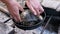 Male Hands Laying a Pond Turtle in a Frying Pan on Grate by an Extinguished Fire