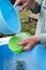 Male hands pour clean water from a ladle onto plastic lids to rinse off the detergent in a country yard, outdoors. Rural