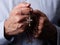 Male hands praying holding a rosary with Jesus Christ in the cross or Crucifix on black background.