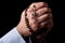 Male hands praying holding a rosary with Jesus Christ in the cross or Crucifix on black background.