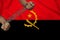 Male hands of a prisoner in iron chains against the background of the national flag of Angola on a beautiful silk fabric, the