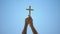 Male hands raising wooden cross to blue sky, religious conversion, baptism