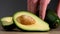 Male hands stack one natural whole avocados on the table next to the cut avocado halves with a whole bone.