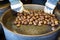 Male hands stirring and roasting delicious organic chestnuts on a gas barrel stove with wooden ladle