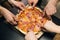 Male hands taking slices of pizza with cheese, tomatoes and ham from food delivery. Group of hungry friends sitting at