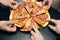 Male hands taking slices of pizza with cheese, tomatoes and ham from food delivery. Group of hungry friends sitting at