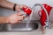 Male hands are washing red cup with sponge under running water in kitchen sink.