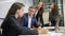 Male head talks to subordinates sitting at table in modern office.