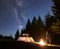 Male hiker enjoyng night camping near tourist tent at campfire under blue starry sky and Milky way