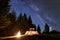 Male hiker enjoyng night camping near tourist tent at campfire under blue starry sky and Milky way