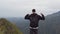 Male hiker reaching up top of mountain and outstretching arms up. Young man tourist with backpack standing on the edge